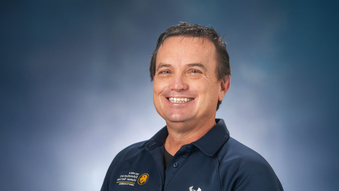 Professional photo of Brian Brumley wearing a dark blue polo shirt against a mottled blue background.